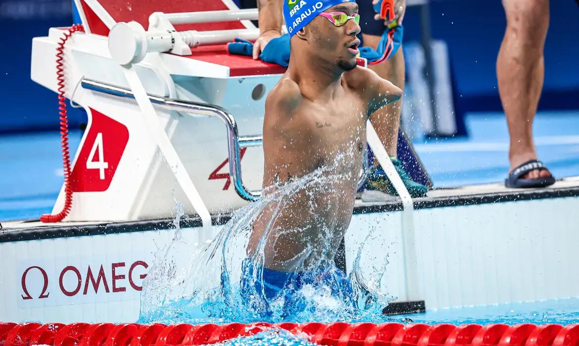 Atleta de natação sai da piscina durante competição, com água espirrando ao redor