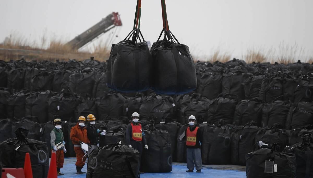 Funcionários especializados manejam enormes sacos plásticos pretos com solo contaminado,
para um "armazém" temporário e improvisado, na cidade de Tomioka, na Província
de Fukushima
