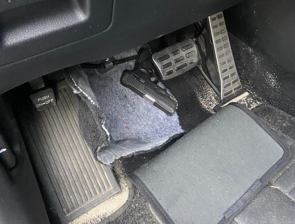 Arma jogada no assoalho de um carro, atrás dos pedais do acelerador e do freio