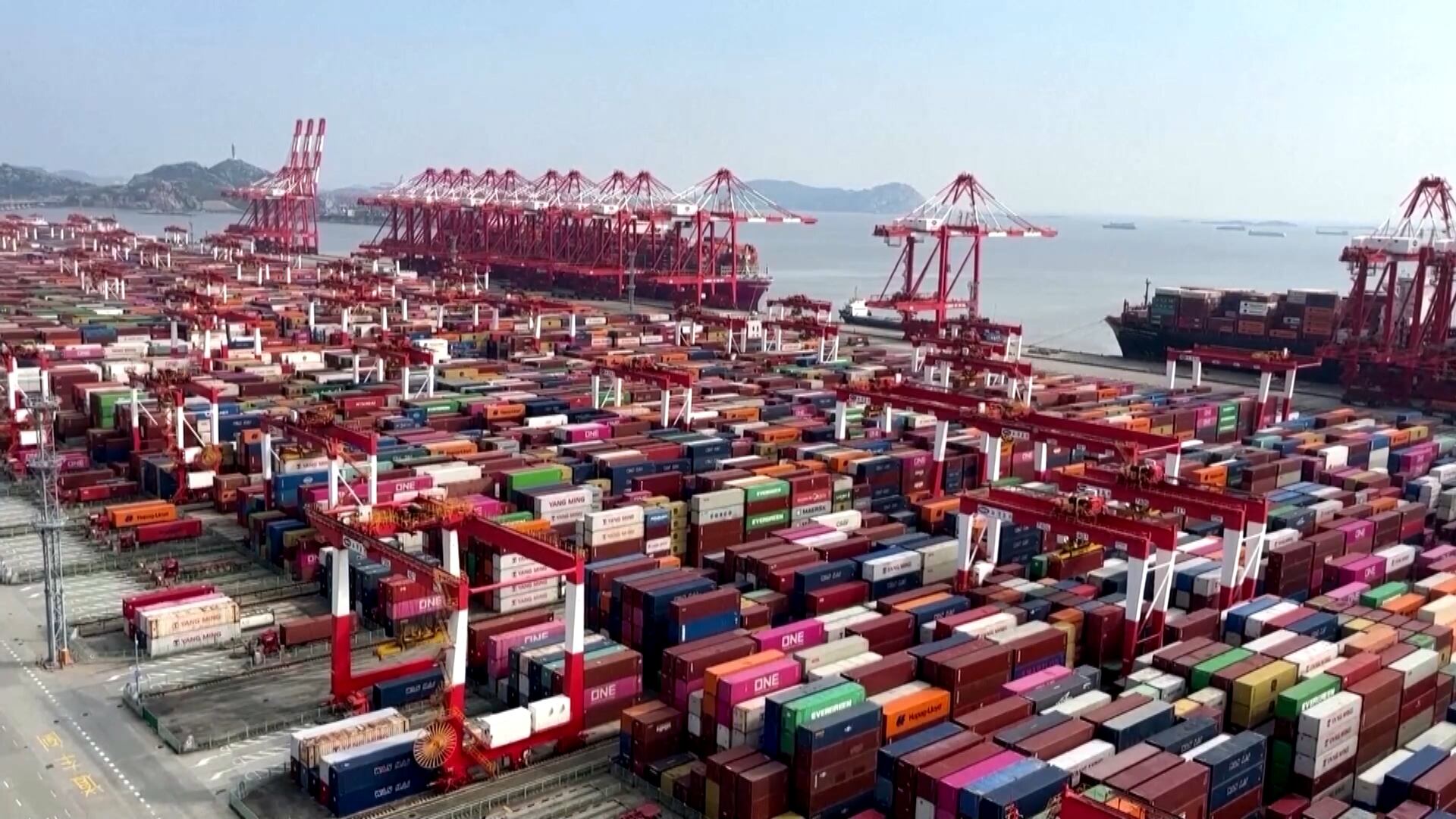 Um porto está lotado de centenas de pilhas de contêineres. Perto do mar, dezenas de guindastes gigantescos permanecem imóveis