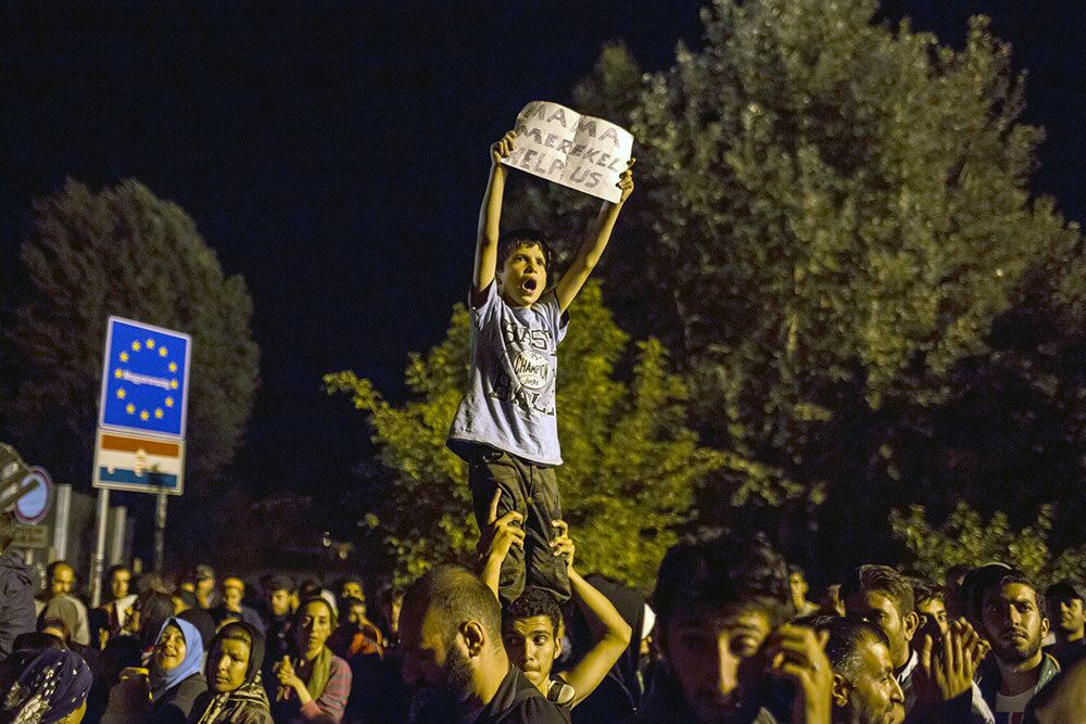Imigrantes impedidos de continuar a longa jornada da Hungria rumo
ao norte, para uma nova vida na Alemanha, protestavam cantando refrões
no fim do dia, e um cartaz dizia: “Mama Merkel, por favor nos ajude!”