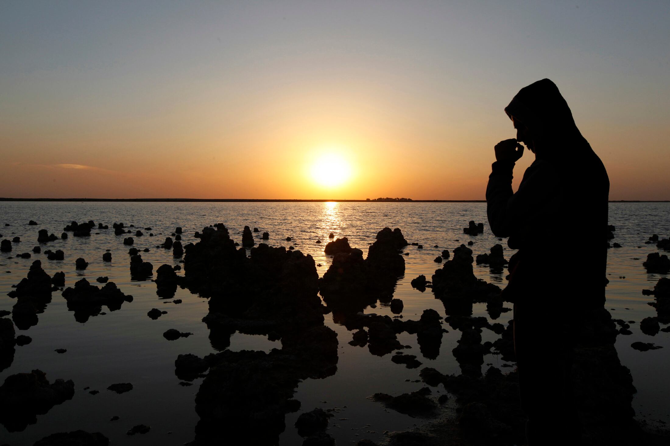 Homem em frente ao lago Sawa, no Iraque. Este é um dos lagos mais conhecidos de Bagdá, apelidado por alguns como "Pérola do Sul", por sua beleza e composição única. O lugar é cercado por um penhasco de dunas de areia, formando um dique natural que mantém a água acima do nível do solo. Como o lago não tem ligação comprovada com qualquer rio ou mar, a fonte de sua água tem sido um mistério para os pesquisadores durante séculos