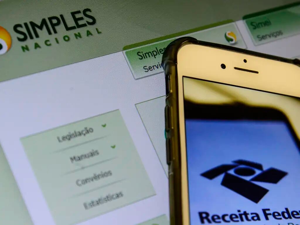 Tela de computador na página inicial do site do Simples Nacional, enquanto celular exibe logotipo da Receita Federal