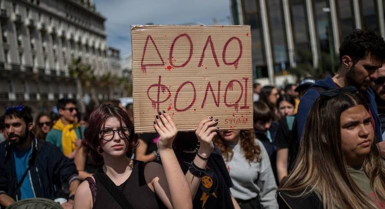 Mulheres seguram cartaz que diz "Assassinos", em grego, durante protesto na capital Atenas
