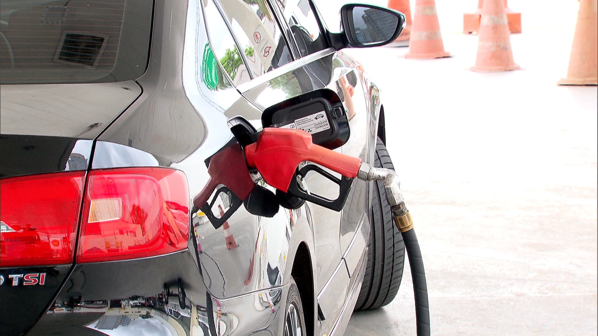 Carro preto em um posto de combustíveis com um bocal de abastecimento vermelho conectado